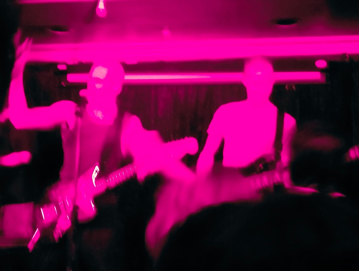 A pink blurry photo of two-thirds of NPCede playing on stage.