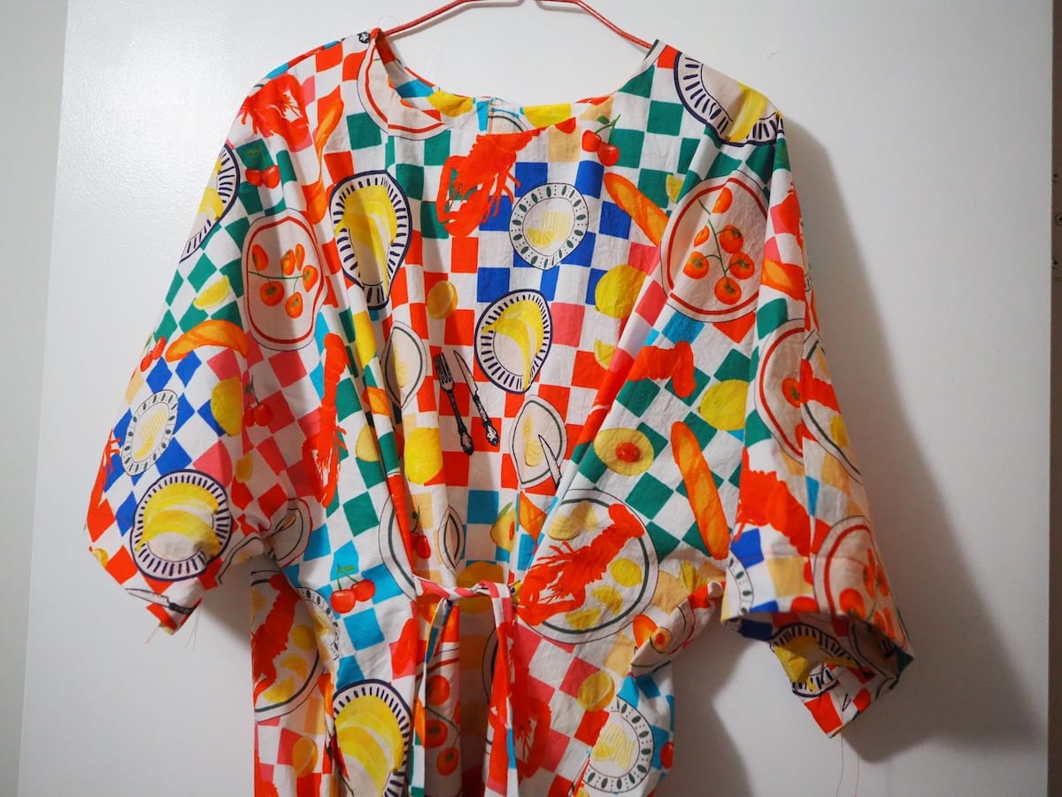 A dress with a bright print, hanging on a coathanger.