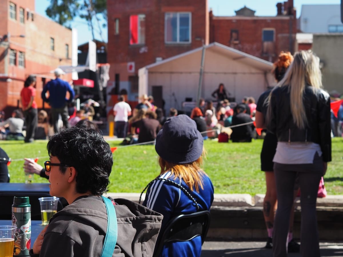 A relaxed and sunny scene of people watching music on a small outdoor stage.