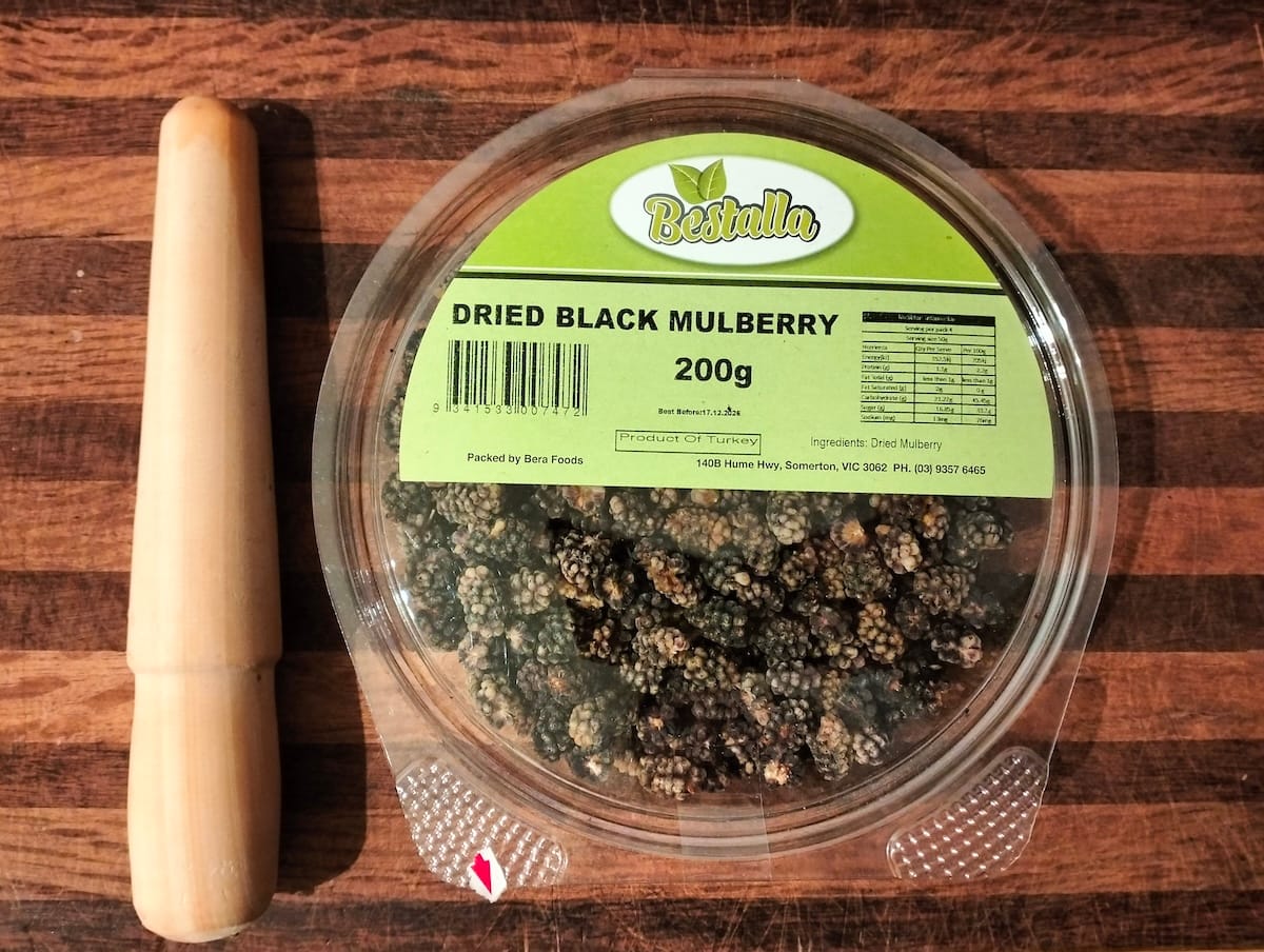 A short spurtle and a container of dried mulberries on a cutting board