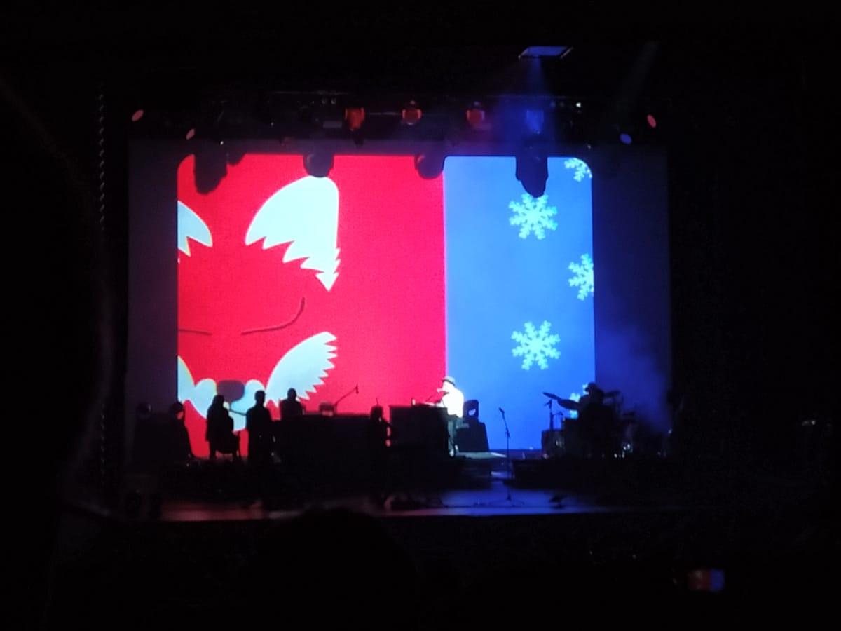 A band on stage, with a large video backdrop showing a fox and snowflakes.