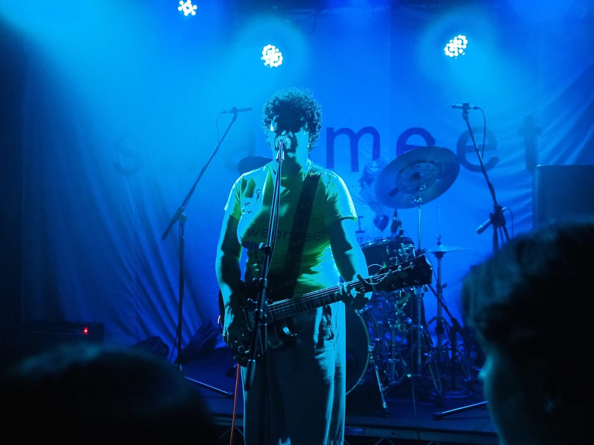 A singer/guitarist on stage with the drummer in the background.