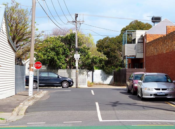 A scene of suburban Melbourne, showing a stop sign at a road junction, houses, parked cars and powerlines.