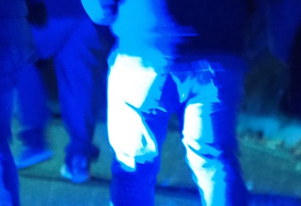 A rear, waist-down view of people walking, bathed in blue light