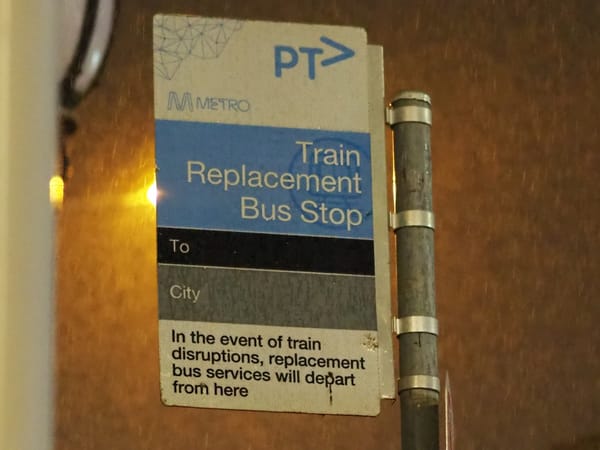 A train replacement bus stop sign, in the rain.