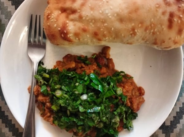 Ful medames with a green garnish with a Turkish bread roll and a fork.