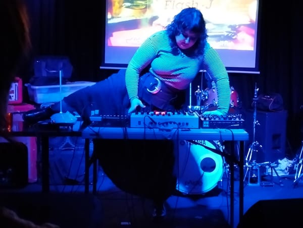 Person on stage playing multiple synths with hands and theremin with leg.