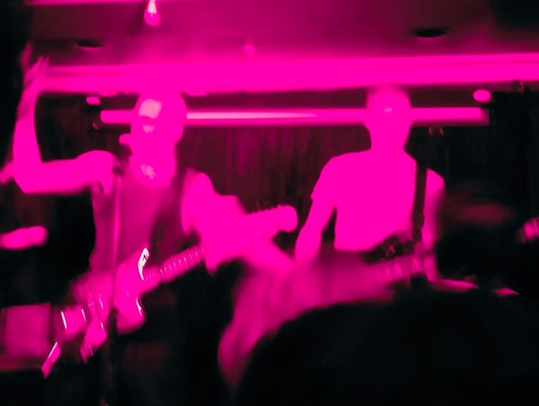 A pink blurry photo of two-thirds of NPCede playing on stage.