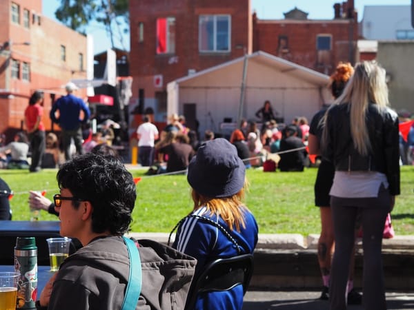 A relaxed and sunny scene of people watching music on a small outdoor stage.