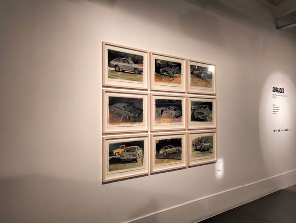 Nine paintings of a 1979 Toyota Corolla on a gallery wall.