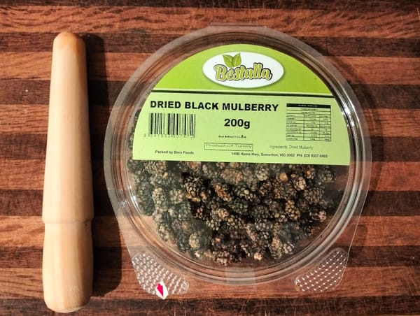A short spurtle and a container of dried mulberries on a cutting board